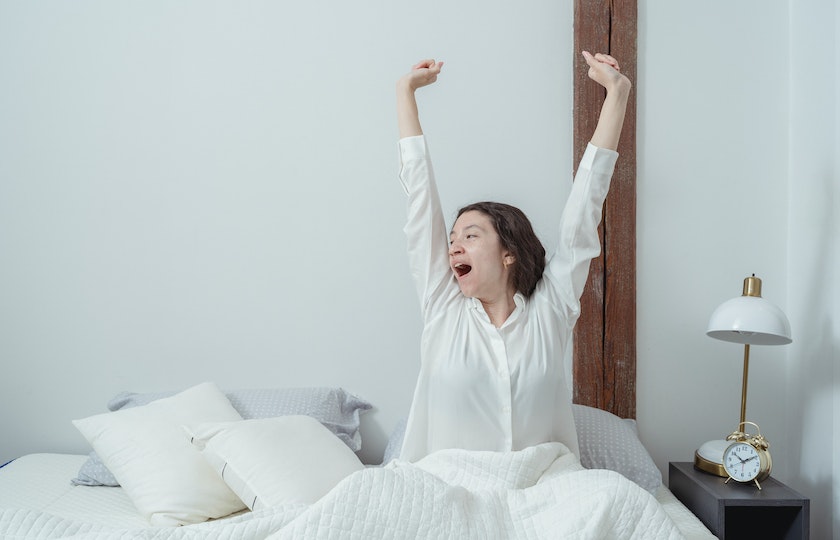 A woman waking up from her bed, representing how to differentiate between morning and evening in the Spanish language.