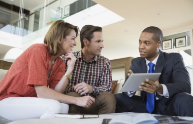 Financial advisor explaining finance terms to engaged couple on a digital tablet, a practical application of Spanish in finance.