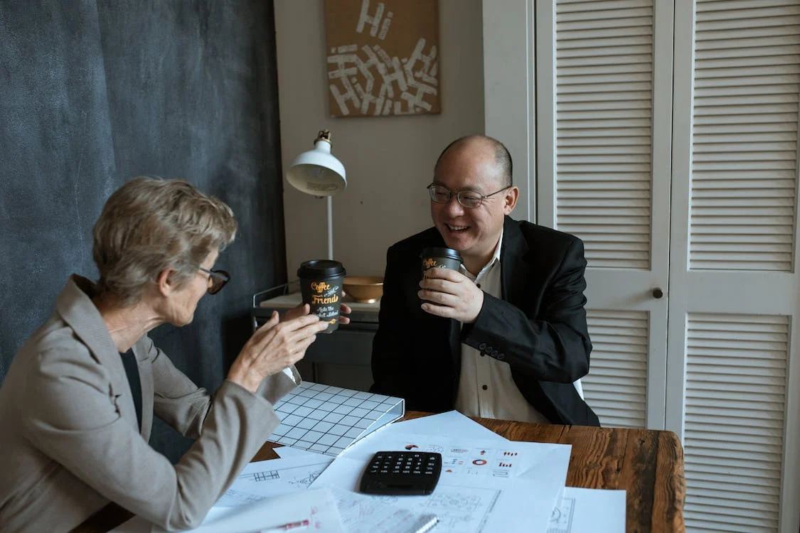 Senior woman and businessman enjoying a coffee break while discussing financial documents, indicative of a personal finance meeting.