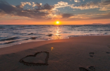 A heart drawn in the sand on a beach at sunset.