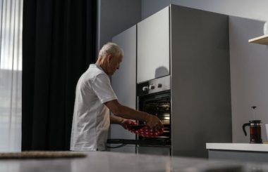 A senior man carefully placing a tray in the oven, a useful scene for learners of Spanish focusing on kitchen appliance vocabulary.