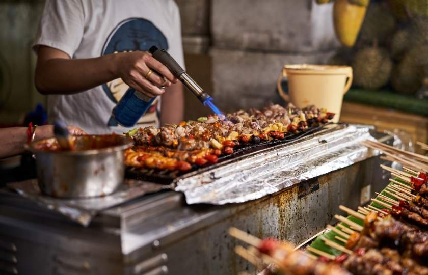 BBQ aficionado using a lighter on skewers, demonstrating Spanish asado skills for authentic barbecuing.