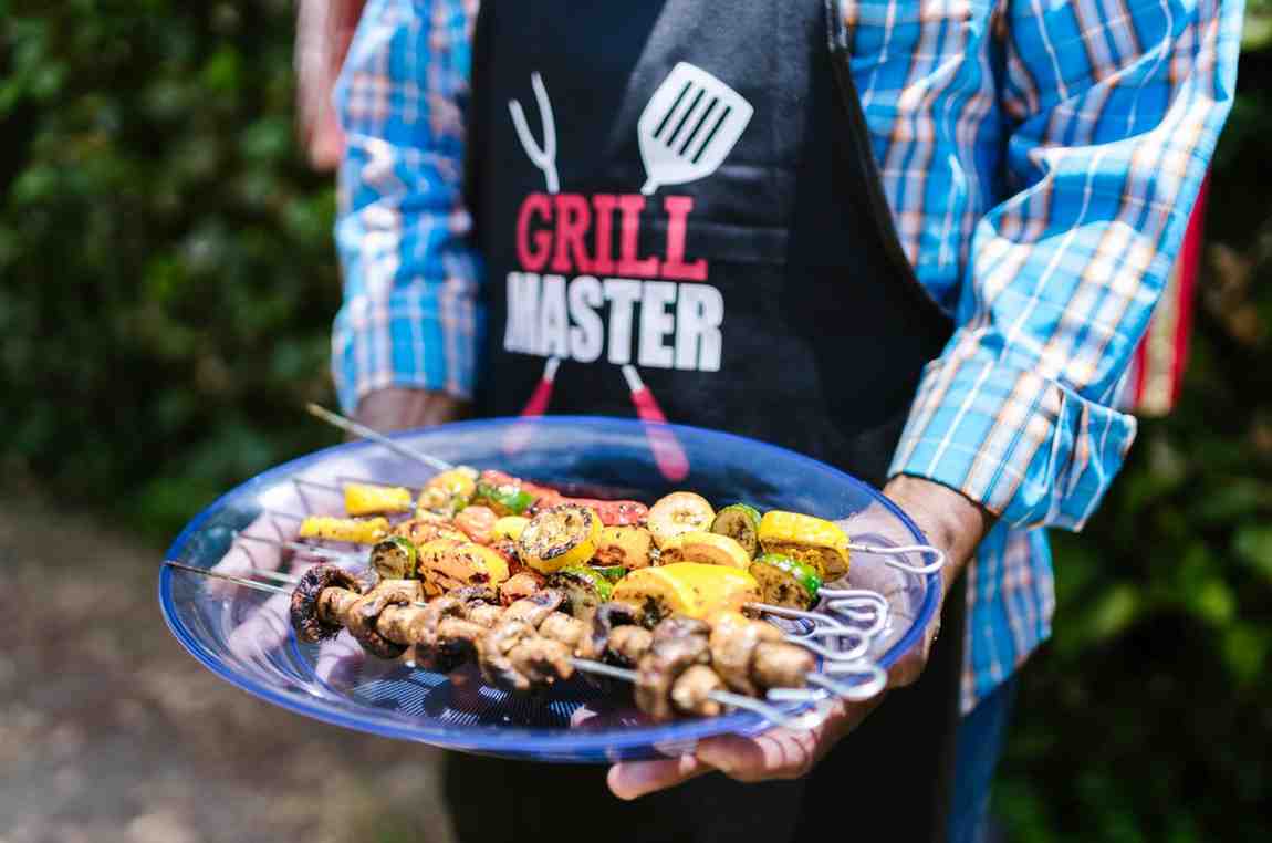 A grill master holding a plate of grilled vegetables, a nod to Spanish BBQ's diverse flavors and terms.