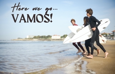 A group of people heading into the sea with surfboards, excitedly shouting 'Here we go, Vamos!' as they embark on an adventurous surfing journey