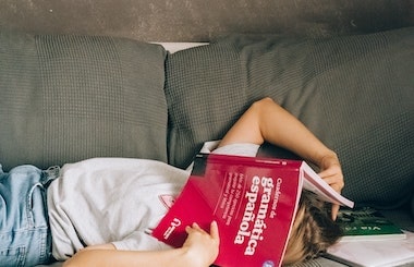 A young boy holding a Spanish grammar book, studying to identify the structure of telling time in Spanish.