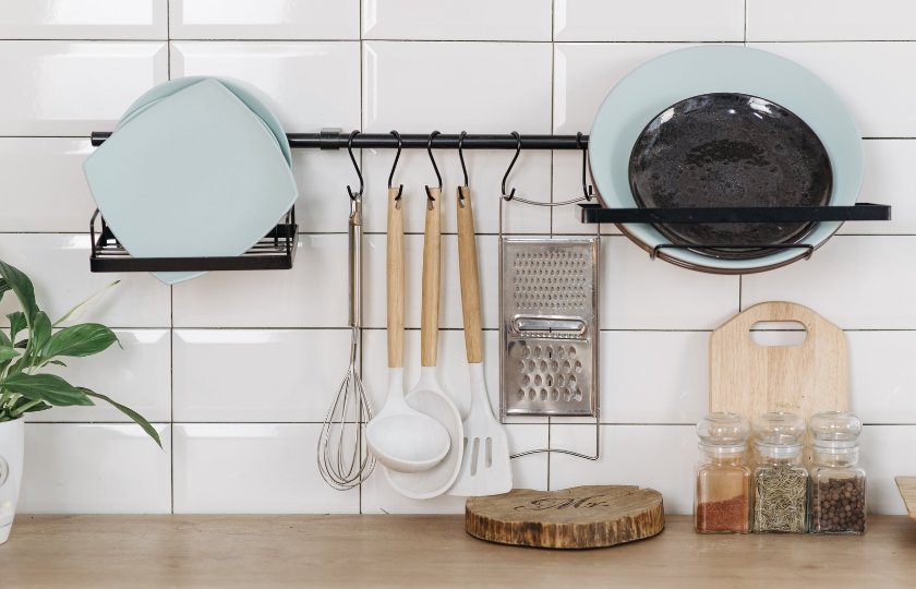 Kitchen utensils hanging on a wall rack, including pans and cooking tools, for Spanish kitchen vocabulary.