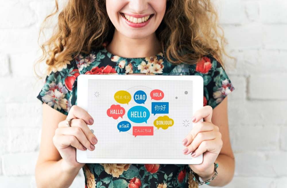 Woman holding a tablet showing greetings in various languages, indicating a guide to Spanish accent marks and special characters for beginners.