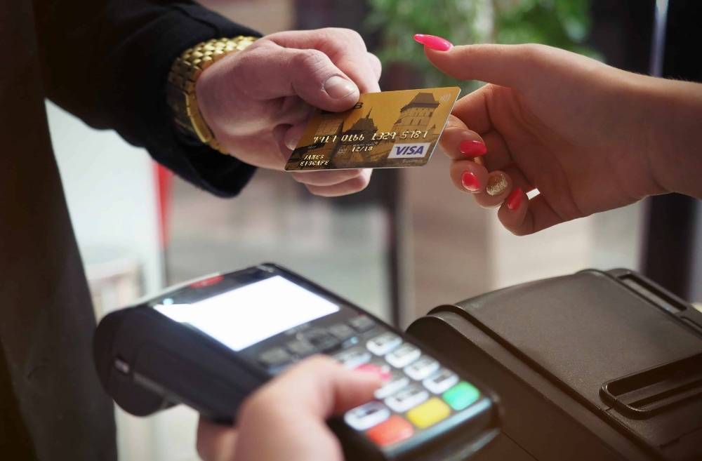 Man handing credit card to woman at payment terminal, illustrating Spanish financial terms, LanguageVibes blog on essential Spanish for beginners.