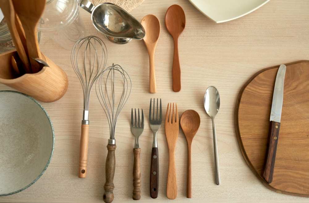 A photo of a variety of wooden utensils on a table including spoons, forks, knives, and a spatula.